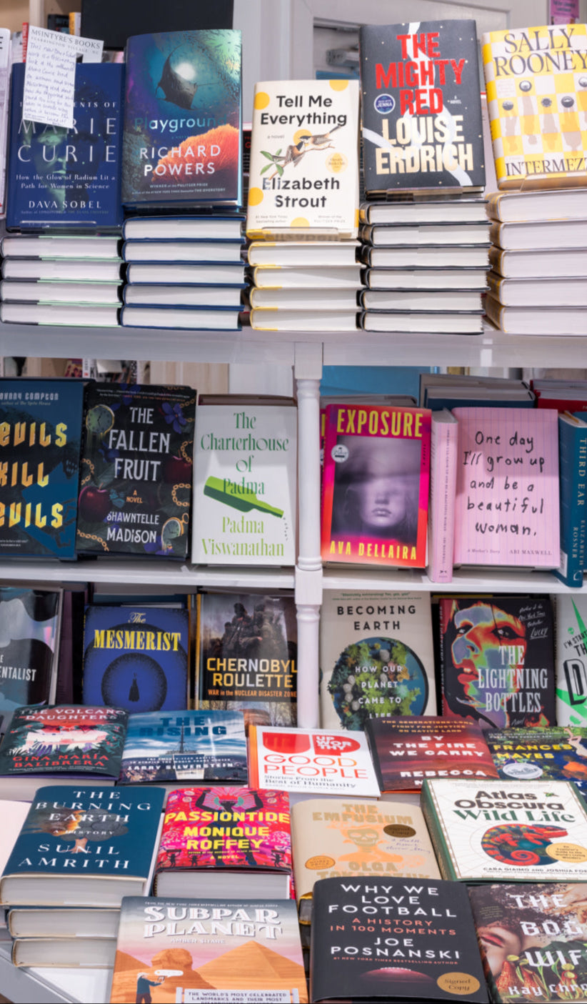 A display of colorful books arranged upright and stacked on a white shelf in a bookstore. Titles such as
