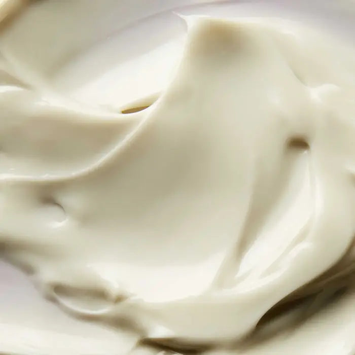 Close-up of a smooth, creamy, beige substance with soft swirls and folds, resembling lotion, cream, or yogurt.