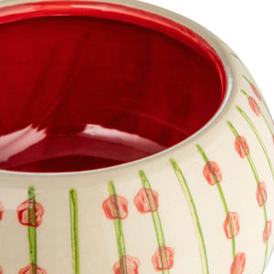 The PLANTER WITH PATTERN by CREATIVE COOP is a hand-painted stoneware ceramic vase that features a rounded bowl shape with a smaller cylindrical base. It is adorned with vertical green lines and small red flowers on a cream-colored background, giving it a vibrant and artistic appearance.