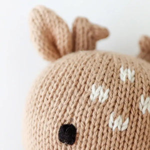 The CUDDLE + KIND - HANDMADE BABY FAWN by CUDDLE & KIND is a charming hand-knit baby fawn plush toy. It resembles a brown deer with two small antlers, round ears, and a petite white tail. The toy stands upright on its legs, facing backwards, highlighting its intricate stitching and soft texture—ideal for fair trade income newborn gifts.