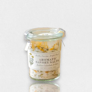 A small glass jar of "Calendula & Chive Savory Salt" by Bella Cucina. The label highlights the presence of Italian Calendula and chive. The jar, which features a metal clasp closure, is filled with a blend of European flat crystal salts and aromatic chive.