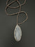 A unique jewelry piece, the ANN LIGHTFOOT Medium Agate Geode Pendant with Snowflake Jasper Strands features a large, polished oval agate geode slice pendant. The stone showcases a distinctive pattern with layered shades of gray, white, and beige that exudes an earthy and natural appeal. The necklace is beautifully displayed against a black background.