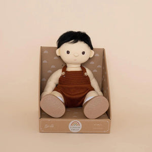 A DINKUM DOLL from OLLI ELLA USA features soft brown hair and comes dressed in a white knit romper paired with brown shoes. This charming doll has an embroidered face with brown eyes, a small nose, and a gentle smile. Its posable body makes it perfect for imaginative playtime, and it is posed standing upright.