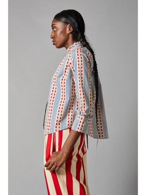 A person with long hair faces away, showcasing the HOPE FOR FLOWERS Frilled Cuff Shirt made from organic cotton, featuring blue and red stripes with dots, paired stylishly with eco-friendly red and white striped pants.