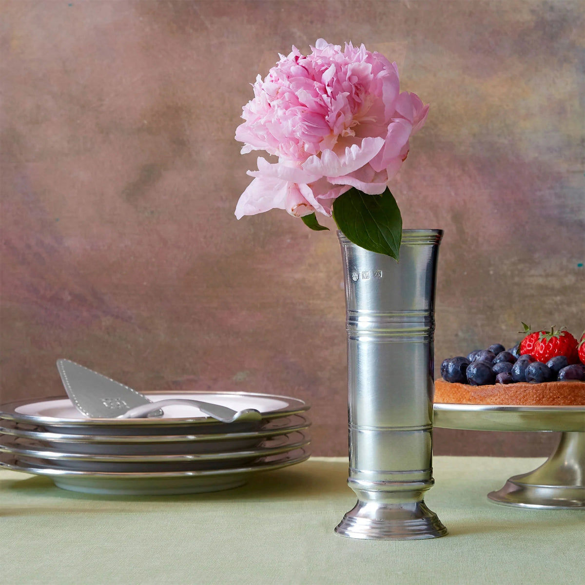 The MATCH Footed Cylinder Pewter Vase by MATCH displays a bouquet of pink, peach, and yellow ranunculus against a white background—an elegant and timeless hostess gift.