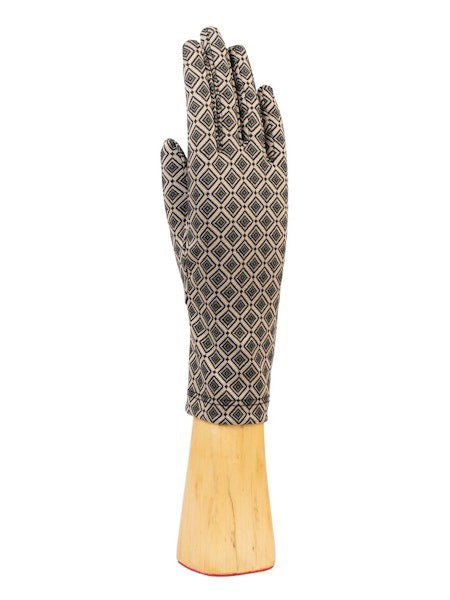 The STRETCH KNIT GEOMETRIC CHECK GLOVES by SANTACANA MADRID WORLD GLOVE COMPANY showcase a stylish geometric design of small red and white diamonds on a black background. Displayed vertically, the gloves rest elegantly on a wooden stand against a plain white backdrop, enhanced by soft wool lining that combines comfort with visual appeal.