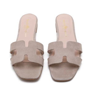 The image depicts the MICHELE LOPRIORE - H SLIDE, a single brown leather slide sandal with an open-toe design. The upper features two wide straps with geometric cutouts. The thin sole appears to be made of light brown wood-like material. Made in Italy by MICHELE LOPRIORE, the sandal is displayed against a plain white background.