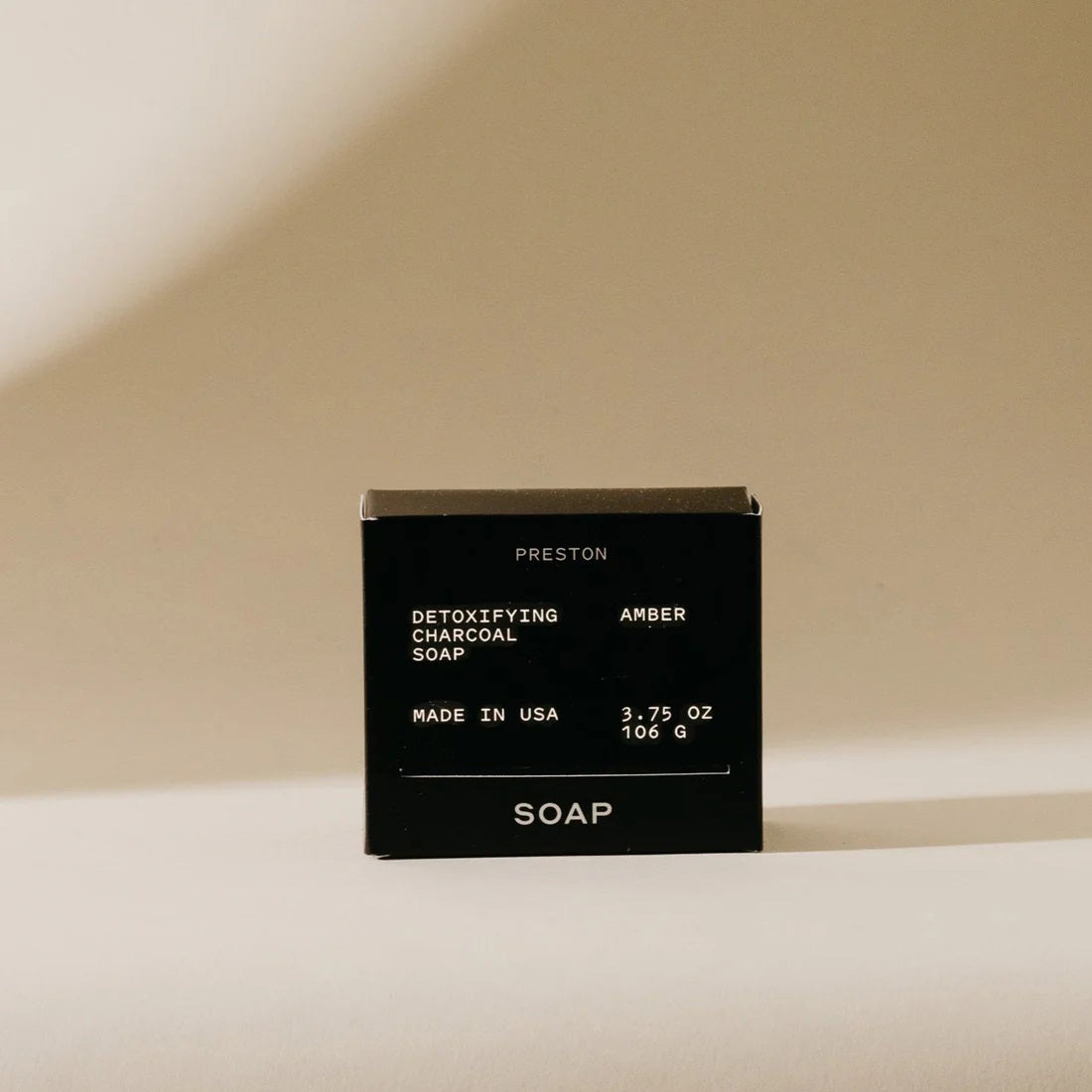 A minimalist arrangement of geometric shapes, featuring a white sphere perched on two black rectangular blocks stacked vertically, with a white cube placed at the base. The objects cast soft shadows against a textured wall, reminiscent of the simplicity seen in PRESTON&#39;s premium bar soap packaging designs.