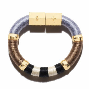 Introducing the HOLST + LEE - COLORBLOCK BRACELET by HOLST & LEE: a circular, multicolored accessory featuring sections of black, beige, and brown materials. This stunning bracelet is embellished with gold rings and a rectangular gold-plated magnetic clasp, seamlessly combining metallic elements with soft textured segments crafted from pearl cotton thread.