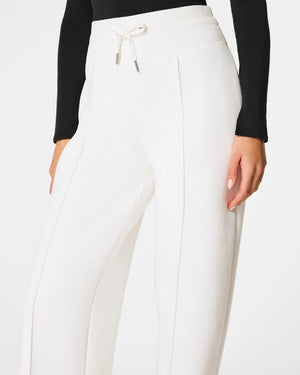 A person wears a black long-sleeve top and SPANX AireEssentials Luxe Straight Leg Pant with a drawstring waist. Relaxed, they pair them with gray shoes featuring black straps. Against a white background, the outfit from SPANX exudes effortless comfort.