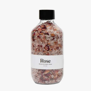 A transparent glass bottle containing a blend of pink and white salt crystals and rose petals, enriched with organic rose and lavender essences. The bottle features a white label that reads "BOTANICAL BATH SOAK - ROSE" from GIFTEN MARKET and is topped with a black cap. Set against a white background, it promises an indulgent bathing experience.