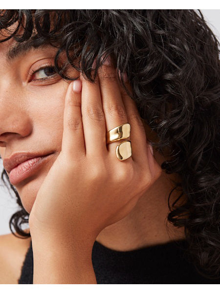 The JENNY BIRD - SOLENE RING features a sleek, modern design with asymmetrical, curved gold-plated ends that wrap around the finger. Its high polish finish enhances its shiny, smooth look, showcased beautifully against a light, neutral background.