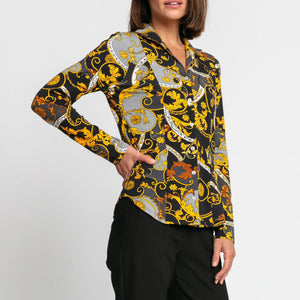 A person is elegantly dressed in the HINSON WU - DONNA SHIRT, showcasing its ornate baroque pattern in black, yellow, gray, and white. Paired with black pants, the stretch polished cotton fabric of this shirt from HINSON WU enhances the sophisticated look against a plain white background.