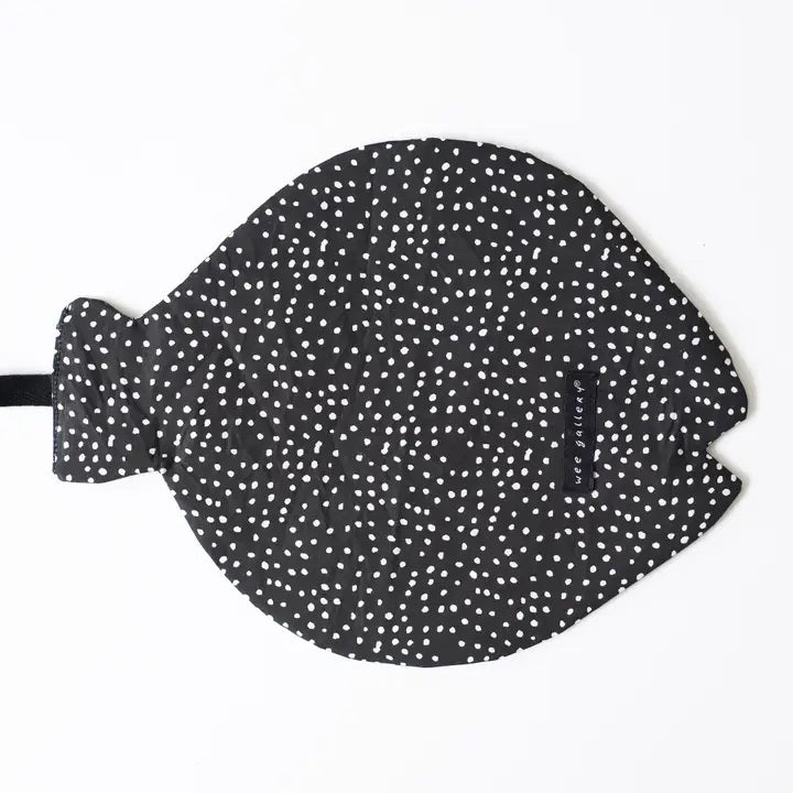 The WEE GALLERY - ORGANIC CRINKLE FISH by WEE GALLERY is a charming black, fish-shaped oven mitt made from organic cotton, featuring white polka dots scattered across its surface. It includes a handle resembling a fish tail and an opening at the side for inserting your hand. Additionally, there's a black tag attached near the middle.