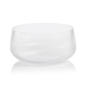 The CONNAUGHT RIPPLED GLASS BOWL - LARGE by ZODAX is an exquisite piece with a clear, textured design featuring a subtle diagonal stripe pattern. Measuring 10.75 inches in diameter and 5 inches in height, this bowl boasts a rounded shape with a wide, open top. Placed on a reflective white surface, its elegant design and transparency are beautifully highlighted, emphasizing its sophisticated dimensions.