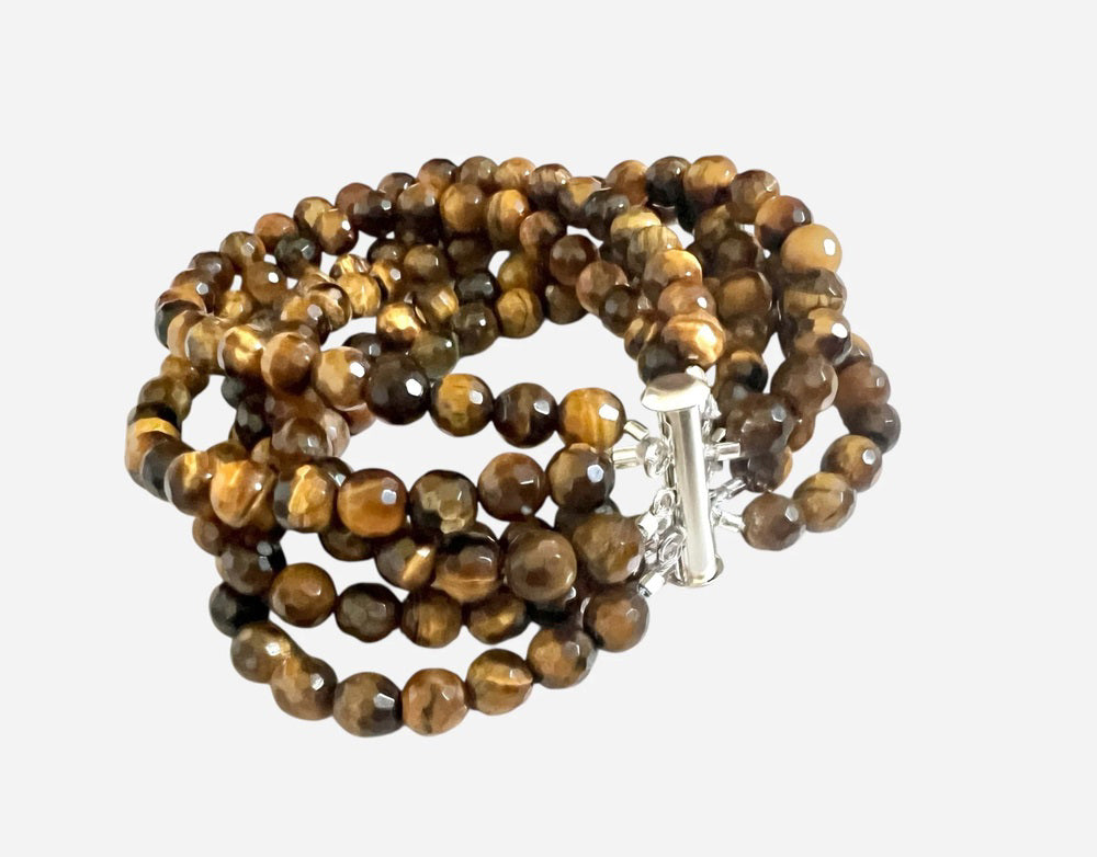 The ANN LIGHTFOOT - TIGER EYE 6 STRAND CUFF BRACELET features polished brown and golden tiger eye beads and a stainless steel clasp, showcased against a white background.