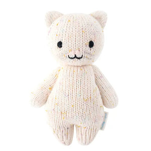 The CUDDLE + KIND - HANDMADE BABY KITTEN by CUDDLE & KIND is a knitted stuffed toy resembling a cat. It features small ears, black button eyes, and a stitched smile. Made from 100% cotton yarn, the light beige kitten has multicolored specks throughout the fabric for a textured appearance. Each purchase of this hand-knit baby animal supports fair trade income.