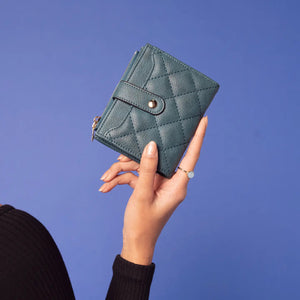 The QUILTED ZIP TOP WALLET by JEN & CO is a teal, small, quilted vegan leather wallet featuring a gold snap closure and a zippered compartment at the top, all set against a plain white background.