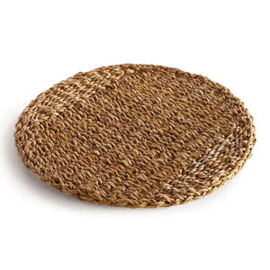 The SEAGRASS ROUND PLACEMAT from NAPA HOME AND GARDEN is made from natural straw fibers and features a braided design with varying shades of light and dark brown, creating a textured pattern. This home decor piece lies flat on a white surface and is perfect for complementing Italian ceramics.