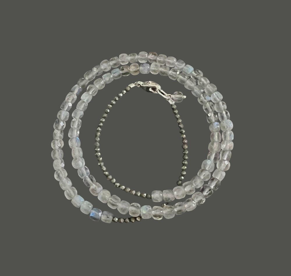 The ANN LIGHTFOOT - TRIPLE WRAP SQUARE CUT LABRADORITE AND PYRITE BRACELET features square and round labradorite beads in a spiral layout with varying transparency for a subtle shimmer, enhanced by a sterling silver clasp for elegance, set against a dark grey background.