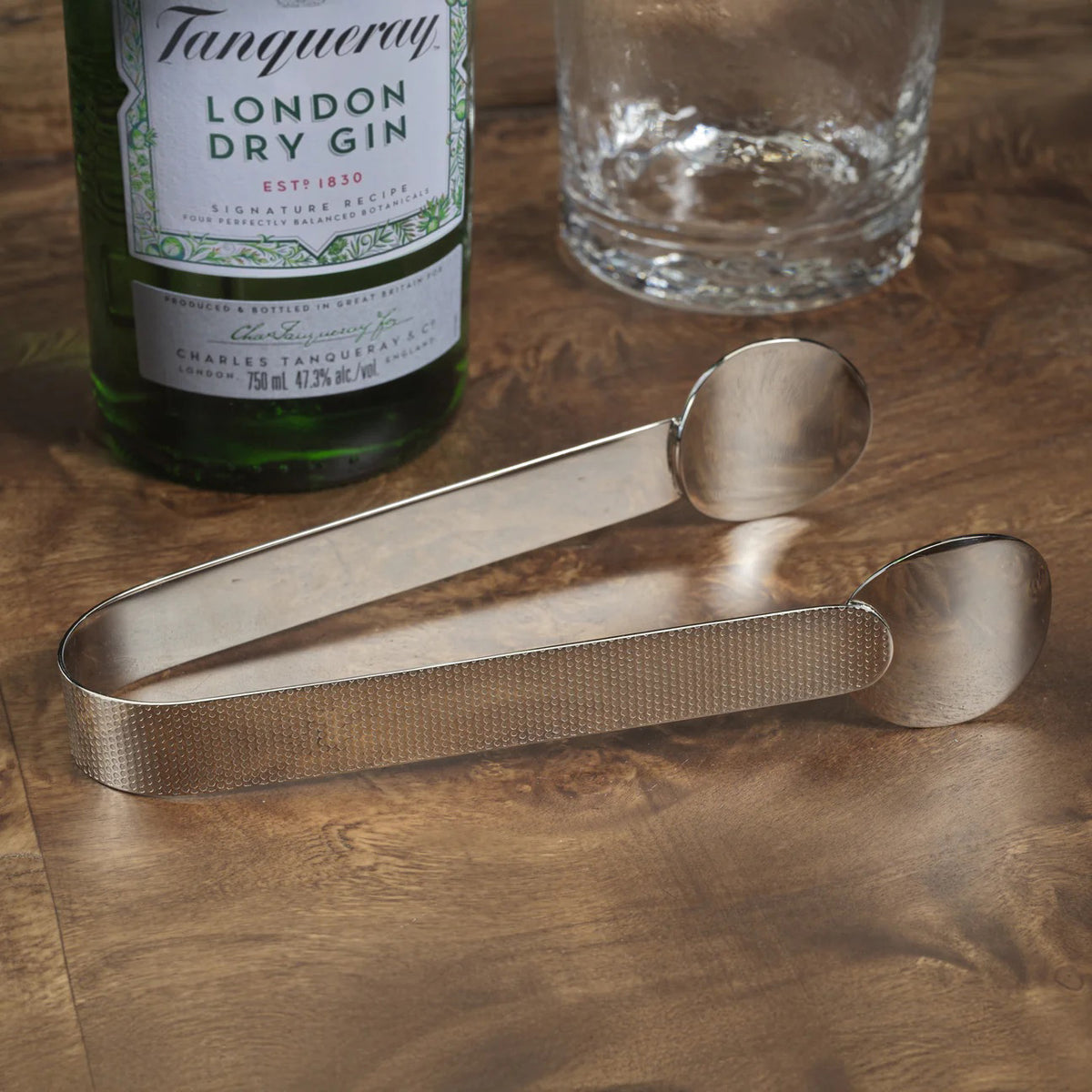 The ZODAX SPIGA TEXTURED ICE TONGS NICKEL, featuring flat, rounded ends and a textured grip, are 7-inch stainless steel tongs made from durable alloy material, shown resting on a white surface.