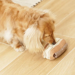 A plush toy named the "LAMBWOLF COLLECTIVE - ECLAIR DOG TOY" by LAMBWOLF COLLECTIVE sits on a white background. The toy features multiple textures with light brown "pastry" sides, a dark brown "chocolate" top, and white "cream" filling, mimicking the appearance of a real snuffle eclair dessert.