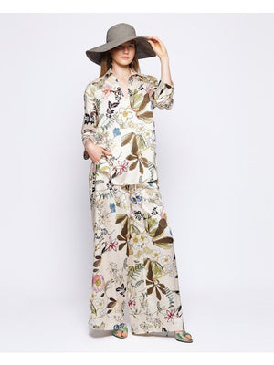 The woman showcases the MIRTO 1956 Botanical Floral Print Fluid Pants with an elastic waistband, complemented by a matching wide-brimmed hat and floral outfit, against a plain background.