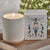 A NUTCRACKER SIBERIAN FIR CANDLE by ZODAX, housed in a minimalist white holder, is placed next to a decorative box featuring nutcracker art. Both items are elegantly arranged on a glittery tray, creating an enchanting atmosphere with fragrance notes that evoke cozy memories.