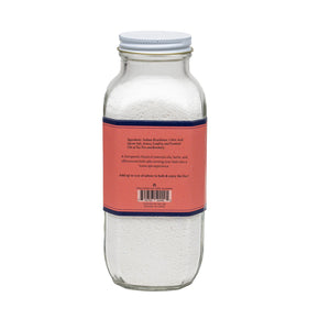 A clear glass bottle labeled "BAUDELAIRE - RECOVER BATH SELTZER 18OZ" with a red and white label. The label highlights that it is handmade, therapeutic, features an effervescent formula, contains all-natural essential oils, and weighs 18 ounces.