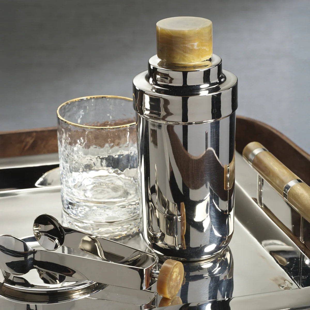 The ZODAX SPIGA COCKTAIL SHAKER - AMBER ACCENTS features a shiny silver body and a light brown, marble-textured alloy resin cap, elegantly showcased against a white background.