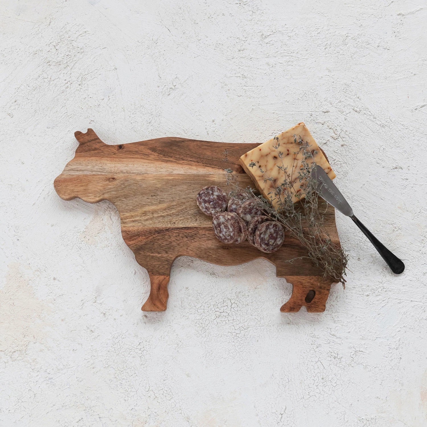 The ACACIA COW CHEESE BOARD by CREATIVE COOP is a delightful cheese board, crafted from acacia wood and shaped like a cow, highlighting the natural grain patterns.