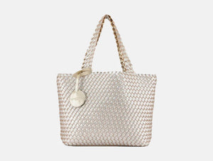 The WOVEN REVERSIBLE TOTE BAG by LINES OF DENMARK is a white tote featuring two shoulder straps and a circular faux-leather tag on one strap. This shopper showcases a textured, interlaced pattern and reversible design, providing stylish and elegant dual styling options. The image background is plain white.