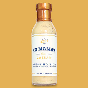 A bottle of YO MAMA'S FOODS' Classic Caesar dressing and dip. The label indicates it is gluten-free, dairy-free, and contains no added sugar. The bottle holds 13 ounces (369 grams) of product. The label features a minimalistic design with a white background and blue and gold accents.