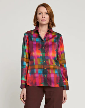 A person with shoulder-length auburn hair is shown from the back, wearing the HINSON WU - Margot Long Sleeve Satin Shirt in Festive Plaid. The multicolored plaid shirt features a collar and includes shades of red, green, yellow, and pink. It is paired with brown pants.