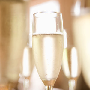 A close-up image of a champagne flute filled with FEARRINGTON VILLAGE's Champagne Wine Class showcases its effervescent splendor. The glass is delicately frosted with condensation, emphasizing its genuine quality. Blurred reflections of similar glasses can be seen in the background, enhancing a festive and sophisticated ambiance akin to exclusive wine classes.