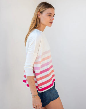 Wearing the MERSEA - CATALINA CREWNECK SWEATER in versatile light pink, a curly-haired individual stands against a plain background. Styled with light-colored pants, hoop earrings, and layered necklaces, they embody the charm of a year-round hero.