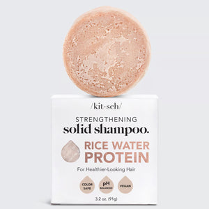 Image of a pinkish-beige solid shampoo bar resting on top of its rectangular white packaging box. The text on the box reads "KITSCH, STRENGTHENING Shampoo Bar, RICE WATER PROTEIN SHAMPOO BAR FOR HAIR GROWTH, For Healthier-Looking Hair, Color Safe, pH Balanced, Vegan, 3.2 oz (91g)." Ideal for damaged hair.