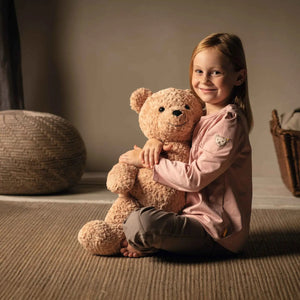 The STEIFF XL JIMMY TEDDY BEAR features a cuddly light brown coat and sits upright against a white background. Its black button eyes, black nose, and small yellow tag in its left ear make it an unforgettable gift to cherish forever.