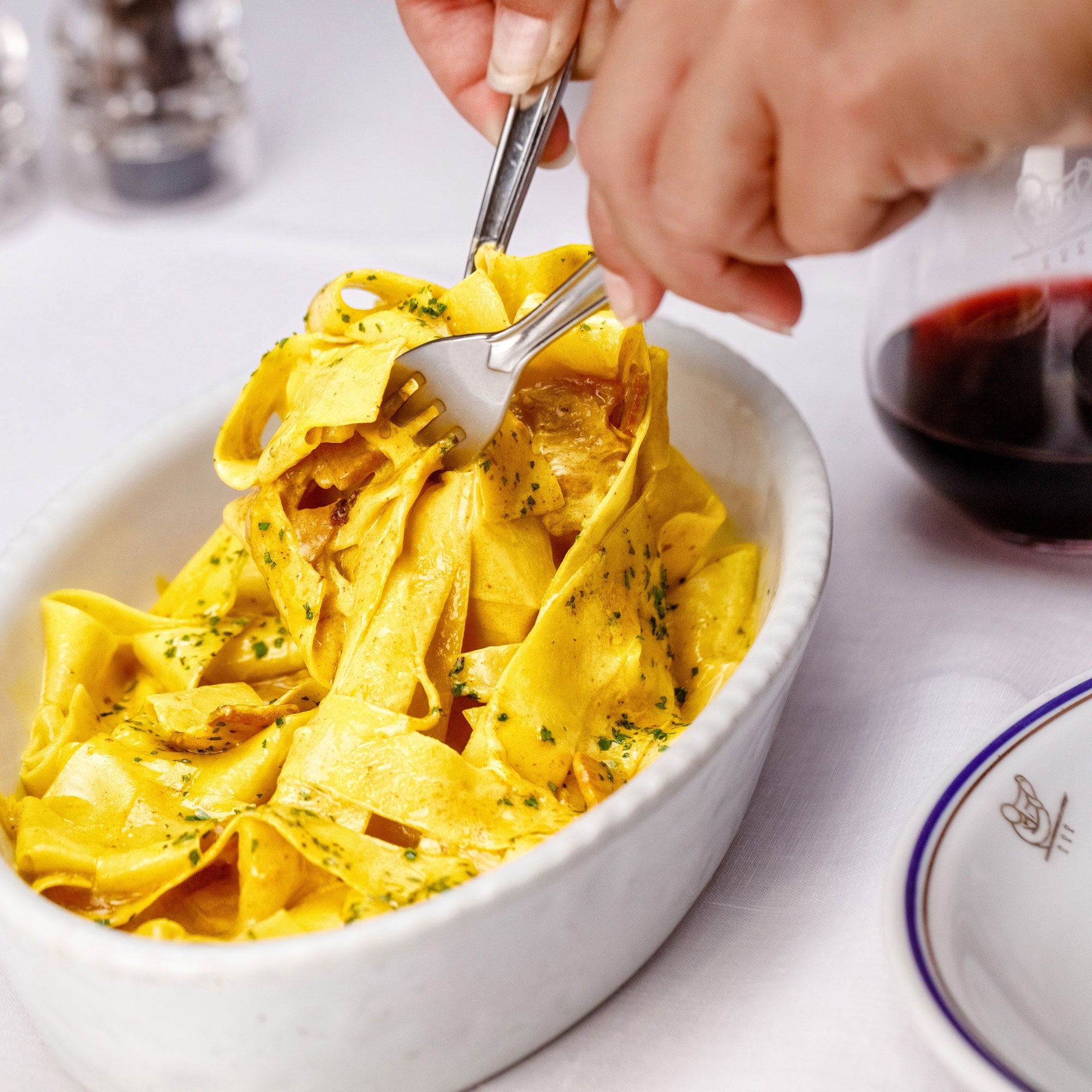 A rectangular box of Cipriani Organic Egg Pappardelle Pasta, produced by Atalanta Corporation and made in Italy, is displayed against a pale background. The light blue packaging with dark blue and white accents features branding details, cooking information, and a small Italian flag denoting its origin.