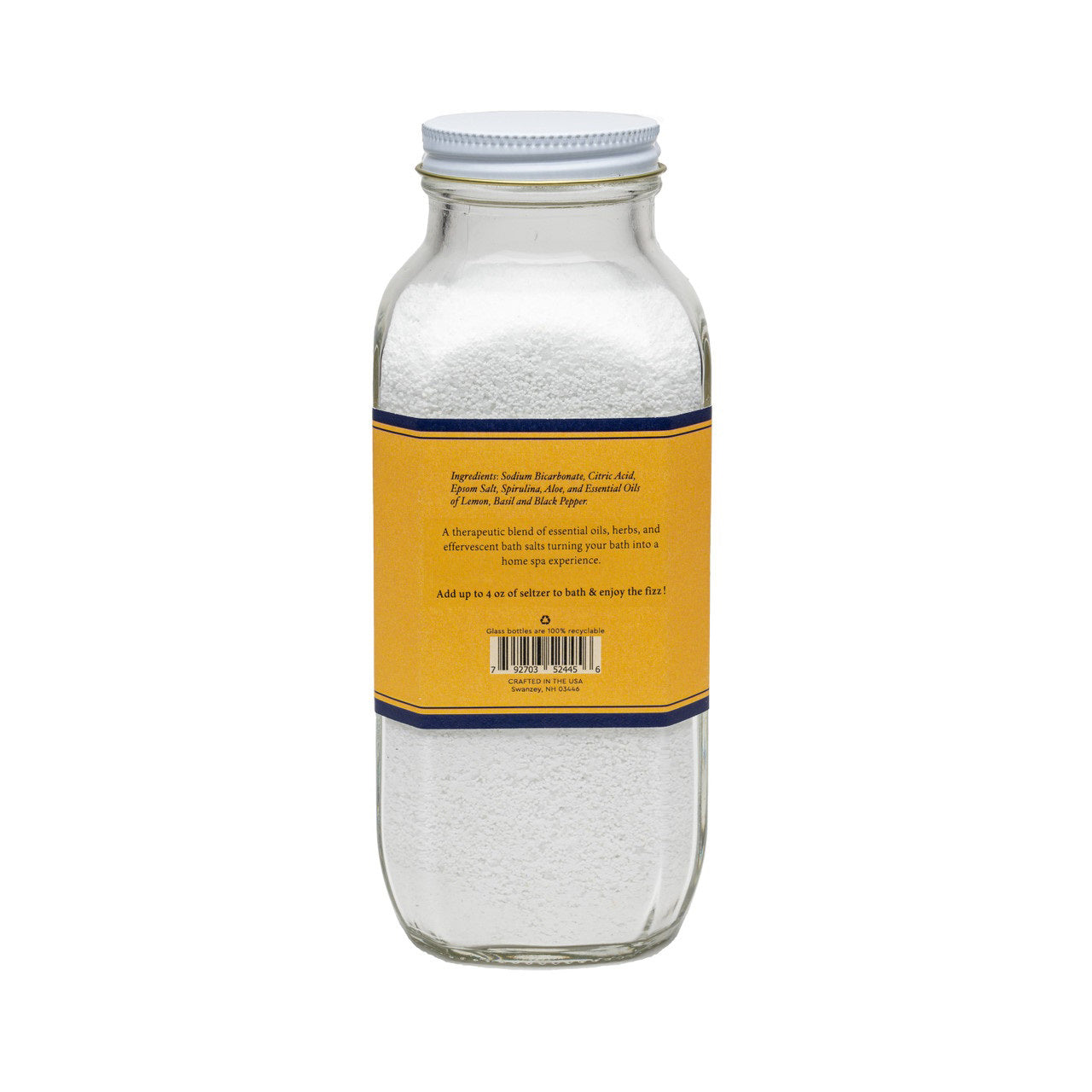 A clear glass jar with a white lid contains white bath salts. The jar's yellow and blue label reads: "BAUDELAIRE - DETOX BATH SELTZER 18 OZ." Additional text indicates it is handmade, therapeutic, all-natural with essential oils and natural ingredients, featuring a proprietary formula.