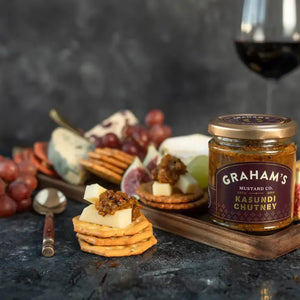 A jar of Graham's Irish Kasundi Chutney with a black and gold label. The label displays the brand name "Graham's," the product name "Irish Kasundi Chutney." This zesty condiment is perfect for a cheeseboard and brings a touch of gourmet elegance to any spread. The jar is sealed with a black lid.