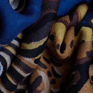 The INOUI EDITIONS - WESTERN SCARF by INOUI features a decorative design showcasing intricately detailed horses in various dynamic poses. This unique scarf presents horses adorned with elaborate patterns set against a deep blue background, creating a visually striking and textured piece of wearable art.