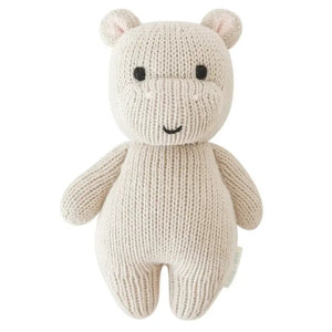 The CUDDLE + KIND - HANDMADE BABY HIPPO by CUDDLE & KIND is a charming, hand-knit stuffed toy featuring a smiling beige hippopotamus with black eyes and small round ears. Its soft, textured appearance and simple, cute features make it an ideal baby shower gift.