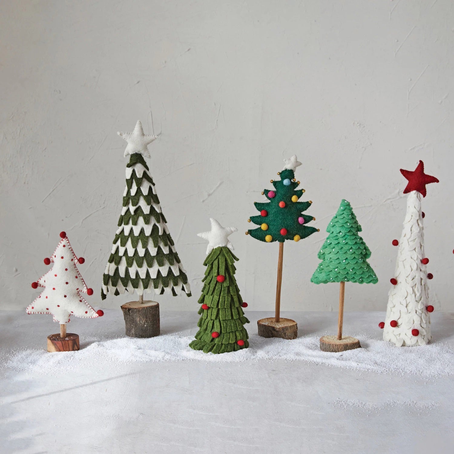 The CREATIVE COOP HANDMADE WOOL FELT TREE WITH POM POMS is a delightful holiday decoration, featuring red dot patterns, red stitching, and playful red pom-poms at the tips. It stands elegantly on a small, round wooden base, making it perfect for festive displays.