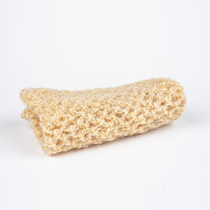 A folded BAUDELAIRE - HORSE HAIR WASH MITT, reminiscent of those used in a Turkish hammam, is displayed against a plain white background. The beige textured cloth appears to be made of knitted or woven material, promising an invigorating clean with its slightly coarse texture.