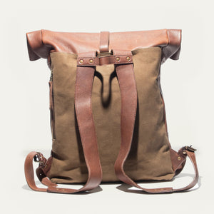 The WILL LEATHER GOODS - ROLL TOP BACKPACK by WILL LEATHER GOODS is open, showing a camera, a red-and-black plaid lining, an Andrzej Sapkowski book, and an old yellowed map inside.