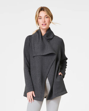 A person with long hair tied back is wearing the SPANX AireEssentials Drapefront Cardigan, crafted in super-soft spacer fabric. They are standing and facing away from the camera against a plain white background, showcasing the essence of everyday layering.