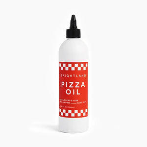 A white bottle features a red label that reads "BRIGHTLAND - PIZZA OIL." The label emphasizes the "Jalapeño & Herb Flavored Olive Oil," highlighting an herbaceous essence. The bottle has a black cap and is displayed against a plain white background.