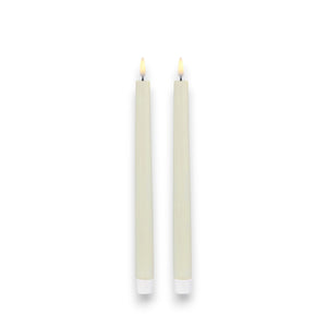 On a plain white background, two ivory UYUNI taper candles by PIFFANY stand lit side by side. Their simple white bases enhance the warm ambiance, creating a subtle yet exquisite luxury setting.