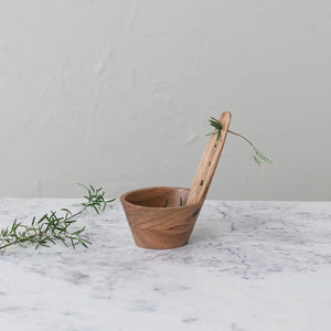 The Creative Coop Acacia Wood Herb Stripper features a long handle with three holes for an ergonomic grip, a deep rounded bowl, and maintains a natural wood grain finish for a rustic appearance.